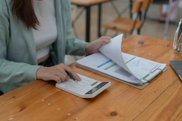 How Much Should a Small Business Pay for Accounting Services? Small business owner using a calculator and reviewing financial statements to work out how much to pay for accounting services